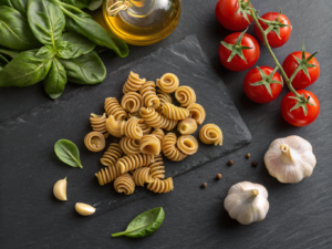 Uncooked bronze-cut trottole pasta with fresh Italian ingredients on a dark slate surface.